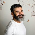 Cheerful man with a beard smiling indoors against artistic background.